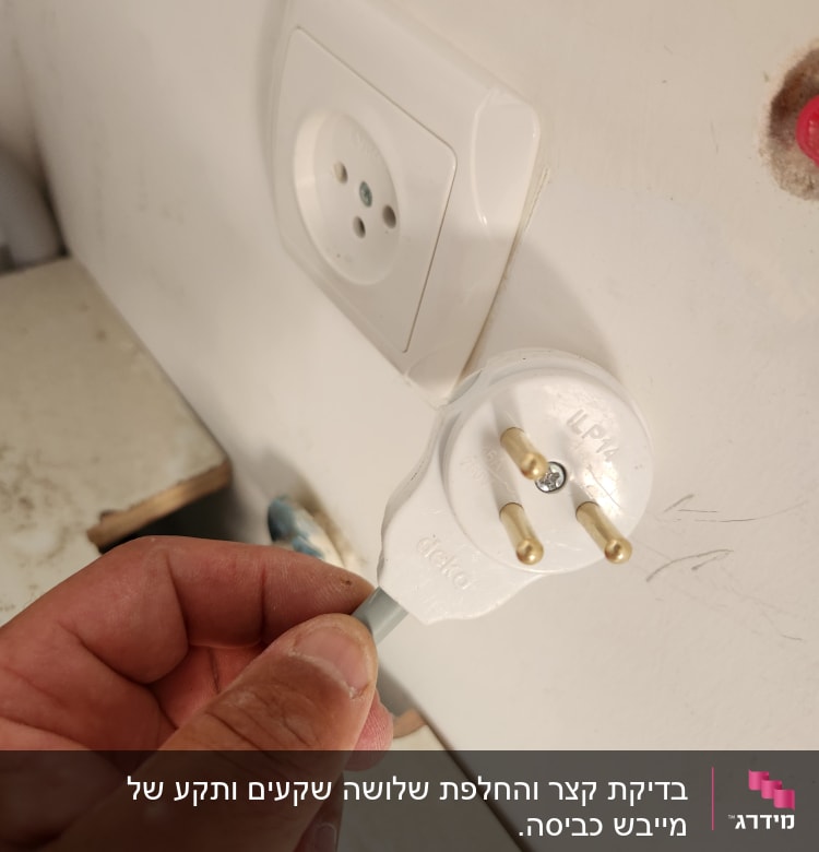 יד מחזיקה תקע חשמלי ליד שקע בקיר